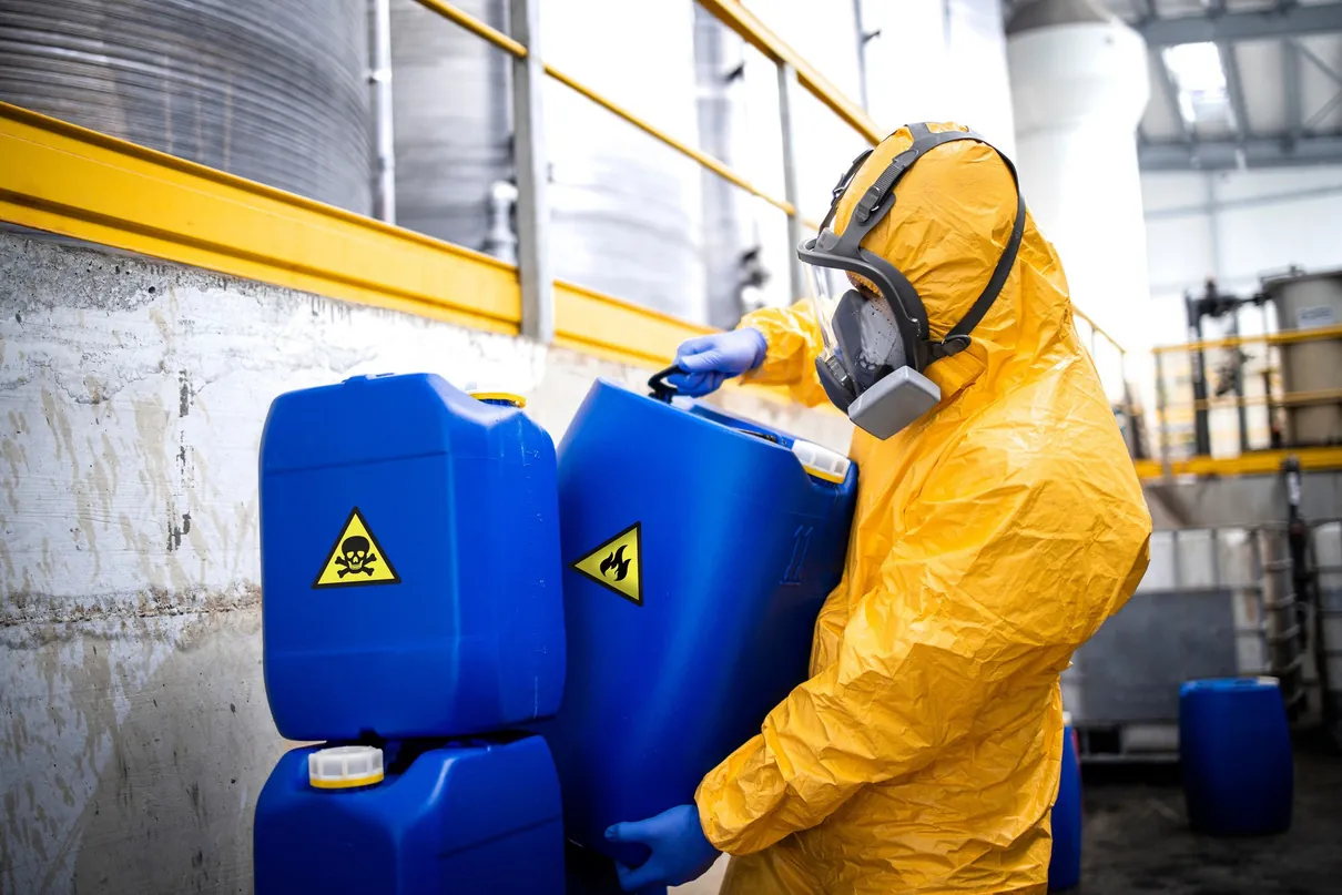 Worker in protective suit handling chemical containers